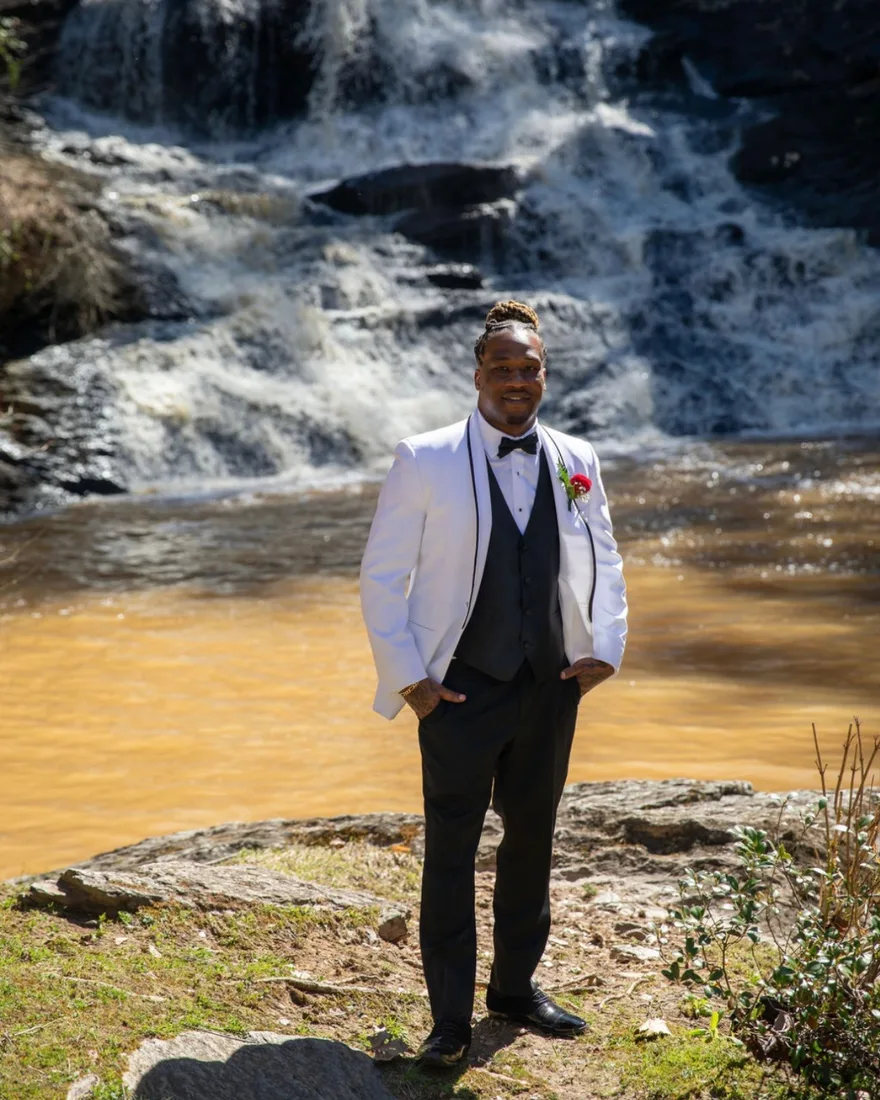 Darryl Jackson in a white tuxedo jacket, standing in front of a waterfall